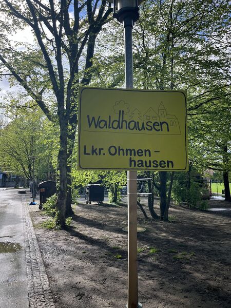 Gebasteltes Ortsschild vor der Waldschule in gelb mit dem Text Waldhausen Landkreis Ohmenhausen.